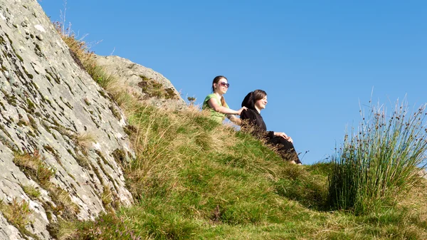 Två kvinnliga vandrare på toppen av berget tar en paus och njuter av en utsikt över dalen, Ben A'an, Loch Katrine, Highlands, Skottland, Storbritannien — Stockfoto