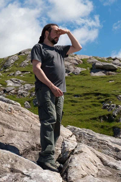 Young handsome caucassian male with dreadlocks enjoying the view on a sunny day trekking in the mountains — Stock Photo, Image