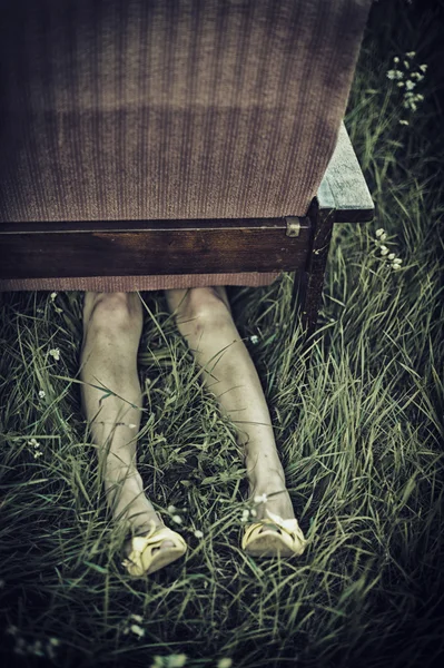 Dirty female legs stickig out from under an armchair in a field, dark mood unusual concept — Stock Photo, Image