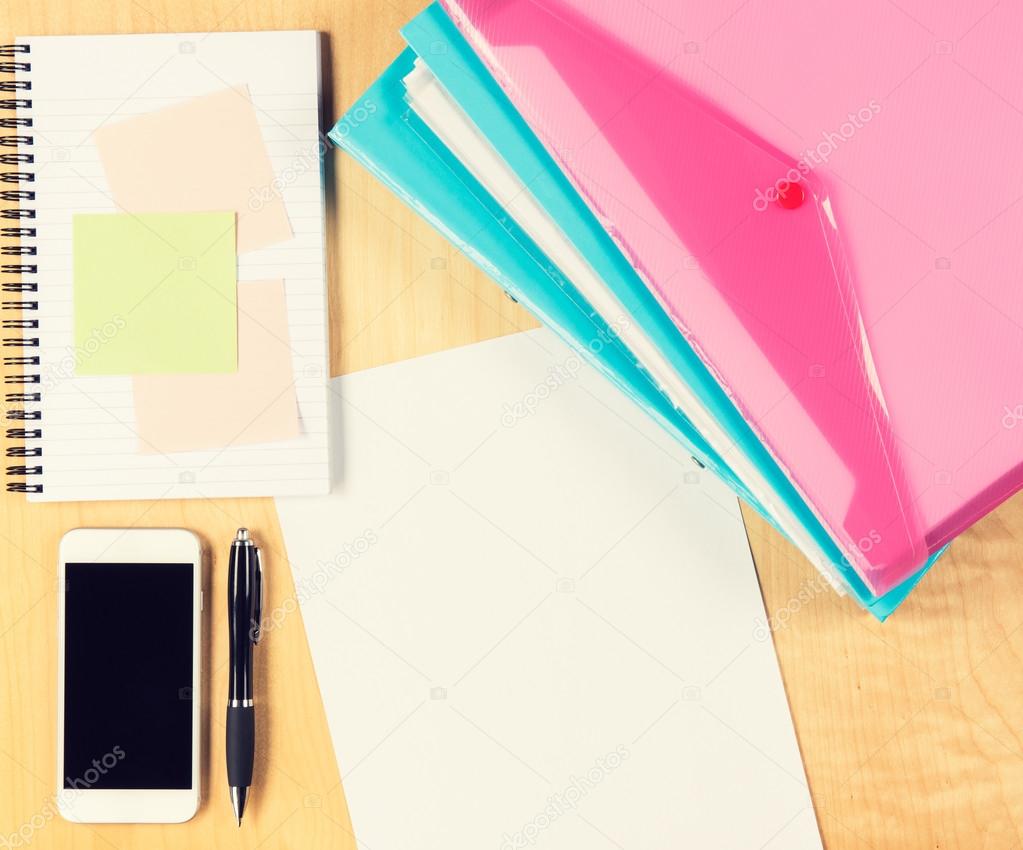 Messy office table with smartphone, notepad and filling folders. View from above with copy space