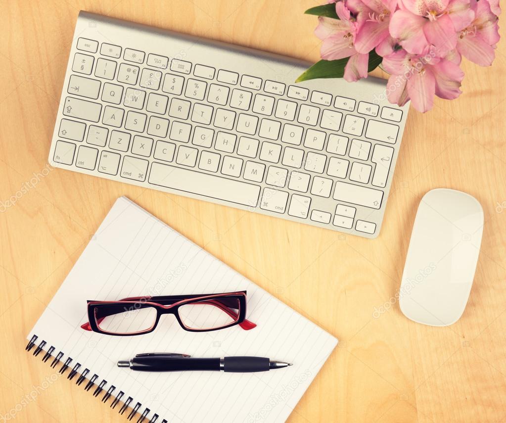 Office table with notepad, computer and reading glasses. View from above with copy space.