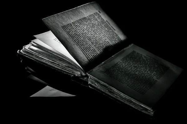 Kontrastreiches Schwarz-Weiß-Bild eines alten Buches auf schwarzer reflektierender Oberfläche — Stockfoto
