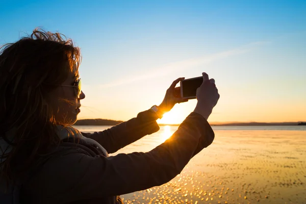 Krásná mladá žena focením ze sebe, selfie, na pláži při západu slunce. — Stock fotografie