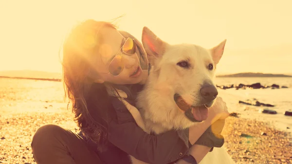 Hippi kız köpekle bir plaj gün batımı, güçlü lens flare etkisi sırasında oynamayı. — Stok fotoğraf