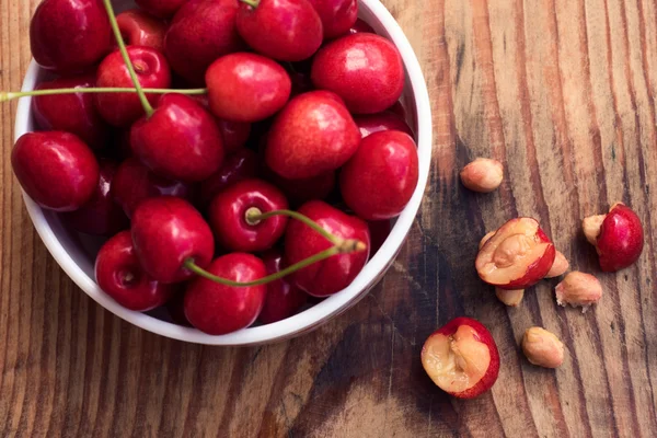 Ripe organic homegrown cherries and stones in a vintage ceramic bowl, on wooden background — Stock Photo, Image