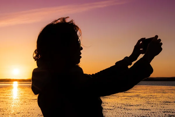 Mulher bonita tirando foto de si mesma, selfie, em uma praia durante o pôr do sol . — Fotografia de Stock