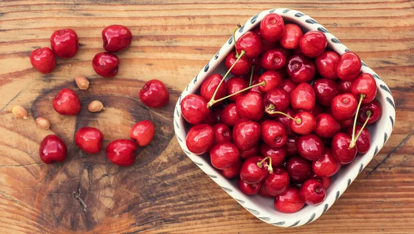 Ripe organic homegrown cherries and stones in a vintage ceramic bowl, on wooden background — Stock Photo, Image