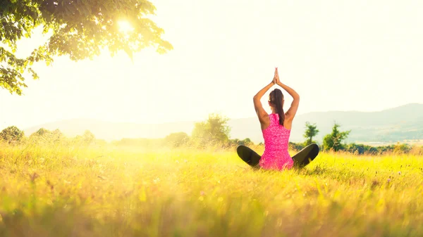 Tânăra femeie atletică care practică yoga pe o pajiște la apusul soarelui, imagine cu flacără de lentile — Fotografie, imagine de stoc