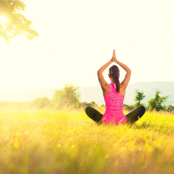 Junge athletische Frau praktiziert Yoga auf einer Wiese bei Sonnenuntergang, Bild mit Linsenschlag — Stockfoto