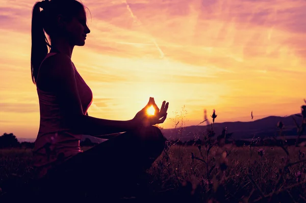 Junge athletische Frau praktiziert Yoga auf einer Wiese bei Sonnenuntergang, Silhouette — Stockfoto