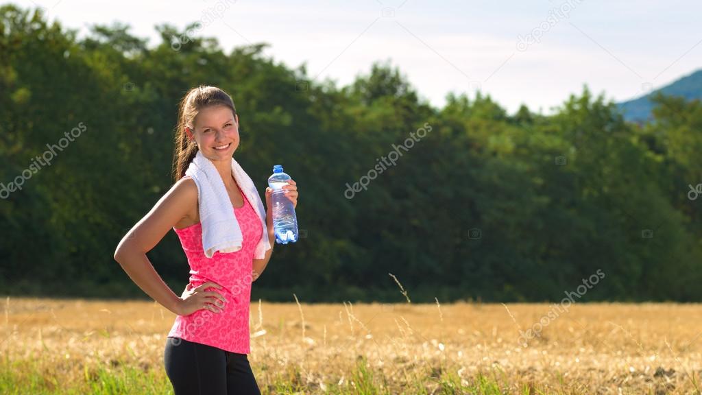 Attractive female taking a break after jogging, holding bottle of water