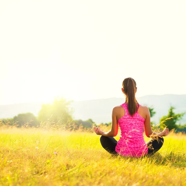 Atletisk ung utövar yoga på en äng på solnedgången, bild med bländning — Stockfoto