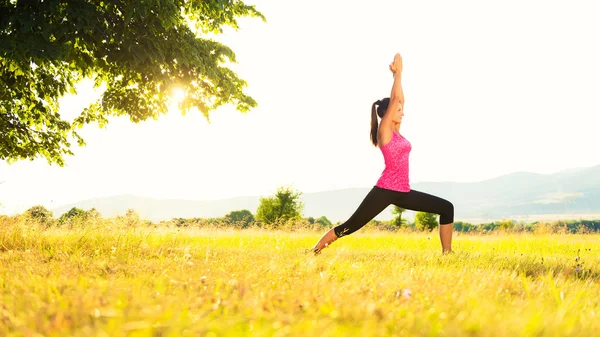 Atletisk ung utövar yoga på en äng på solnedgången, bild med bländning — Stockfoto