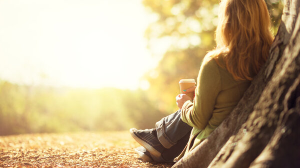 Autumn concept, anonymous woman enjoying takeaway coffee cup on sunny cold fall day