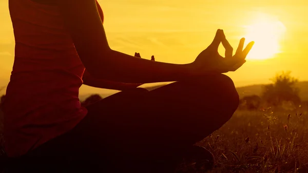 Atletische jongedame beoefenen van yoga op een weide bij zonsondergang, silhouet — Stockfoto