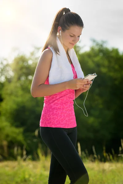 Attraktiv kvinna tar en paus efter jogging, anläggning smartphone — Stockfoto