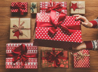 Woman organising beautifuly wrapped vintage christmas presents on wooden background, view from above clipart