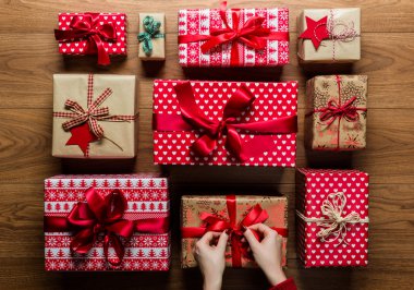 Woman fixing a bow on beautifuly wrapped vintage christmas presents on wooden background, view from above clipart