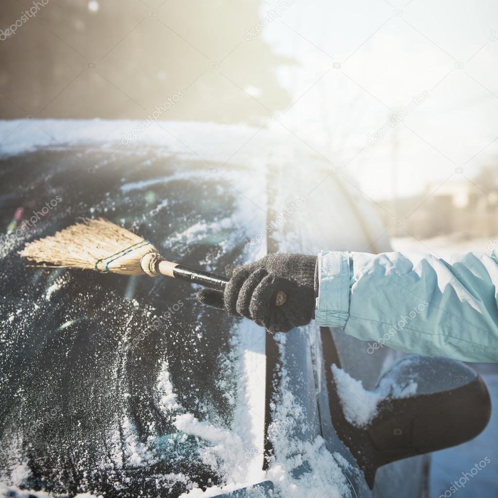 Transportation, winter, weather, people and vehicle concept - woman cleaning snow from her car with a broom