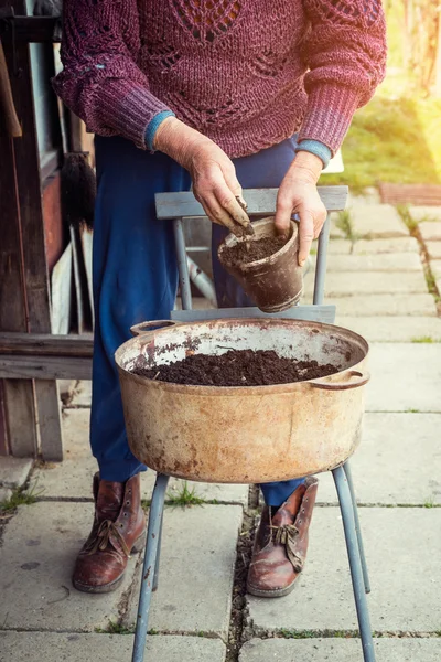 Old woman filling a pot with fresh soil. Symbol of spring and clean eating concept. — Stock Photo, Image