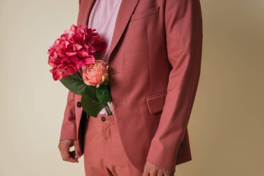 Sarı arka planda bir fotoğraf stüdyosunda, pantolonunun içinde çiçekler olan yakışıklı genç bir adam pembe bir takım elbise ve tişört giyiyor..