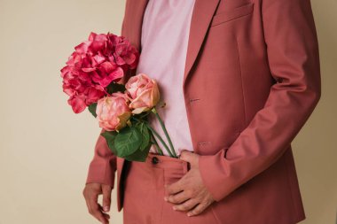 Sarı arka planda bir fotoğraf stüdyosunda, pantolonunun içinde çiçekler olan yakışıklı genç bir adam pembe bir takım elbise ve tişört giyiyor..