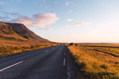 İzlanda 'da güneşli bir günde, arka planda tepe olan asfalt bir yol.