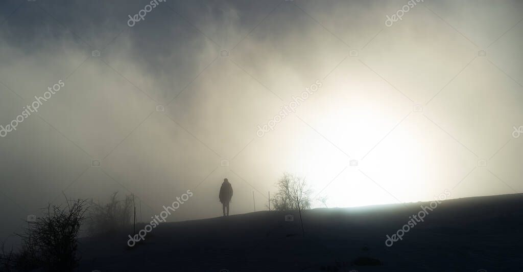 A woman walks towards the sun in the blown fog on top of a mountain on a cold winter day in southern France