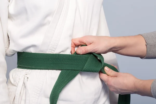 Hands of a parent who helps a child to tie a green belt — Stock Photo, Image