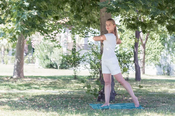 Blondýnka mladá žena dělá jógu v parku — Stock fotografie