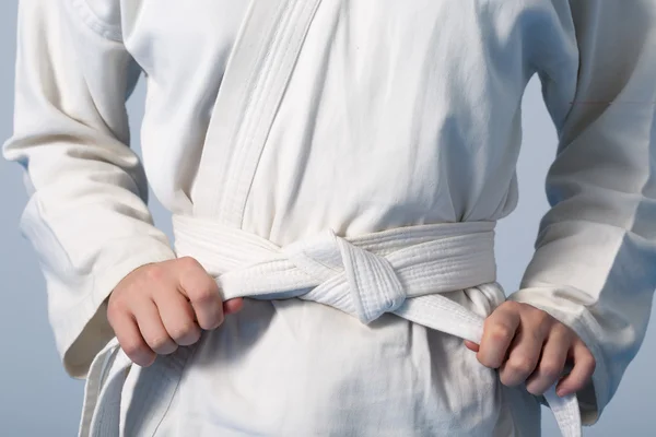 Руки затягивают белый пояс на подростке, одетом в кимоно — стоковое фото