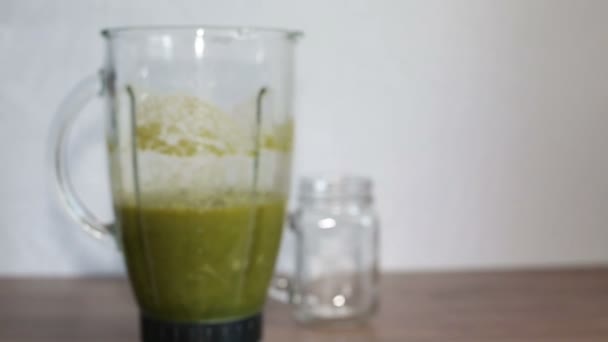 En mixerskål med gröna friska smoothie och en murare burk på ett träbord — Stockvideo