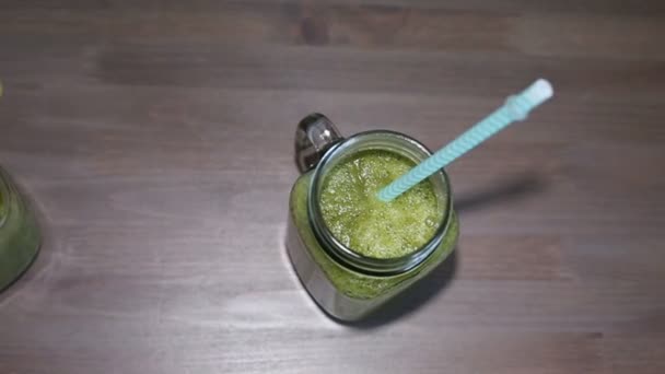 Zelené koktejly v mason sklenice s trubicemi na dřevěný stůl — Stock video