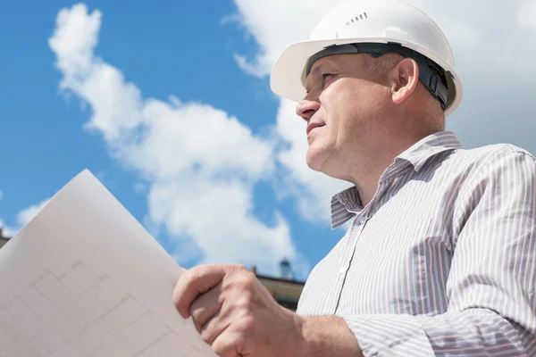 Un obrero de la construcción con casco blanco sosteniendo planos sobre un fondo con cielo azul — Foto de Stock