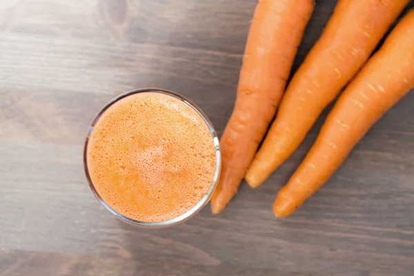 Ett glas friska morot smoothie med morötter på trä bakgrund — Stockfoto