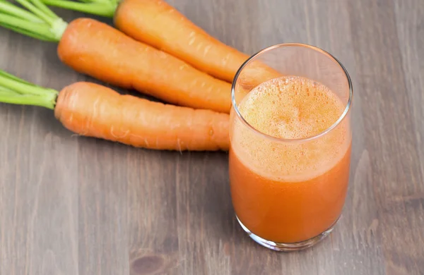 Ett glas friska morot smoothie med morötter på trä bakgrund — Stockfoto