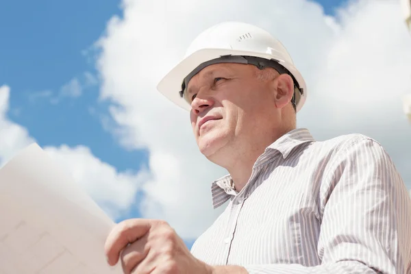 Un obrero de la construcción con casco blanco sosteniendo planos en las manos — Foto de Stock