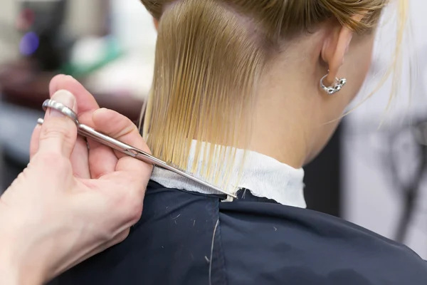 Peluqueros mano sosteniendo tijeras haciendo corte de pelo para una mujer rubia cliente — Foto de Stock