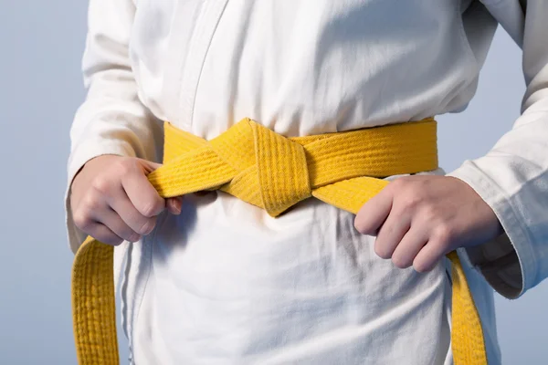 Hands tightening yellow belt on a teenage dressed in kimono — Stock Photo, Image