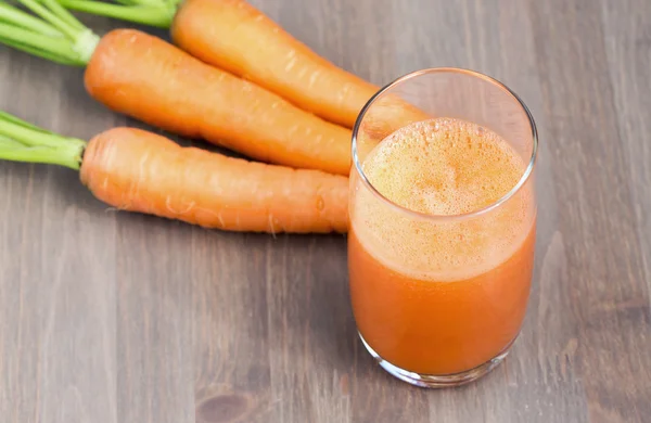 Friska morot smoothie i ett glas med råa morötter på en trä bakgrund — Stockfoto