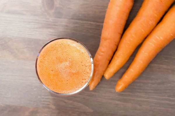 Healthy carrot smoothie in a glass and raw carrots on a wooden background