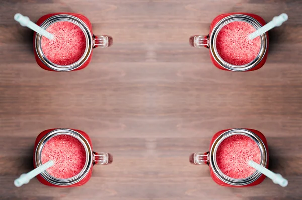 Uma vista rasa superior de uma melancia smoothies em um pedreiro frascos com tubos em fundo de madeira — Fotografia de Stock
