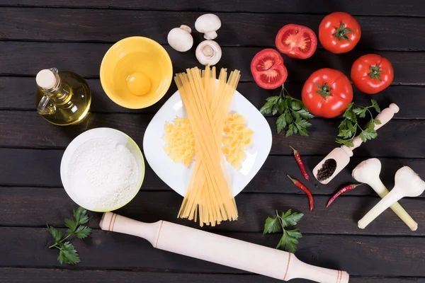 Raw pasta, tomatoes,mushrooms, flour and egg on black wooden table background, top view — Stock Photo, Image