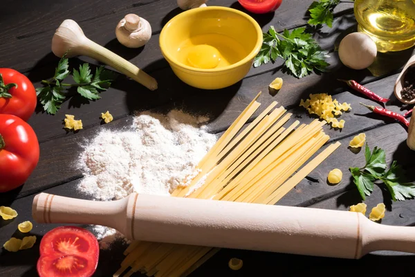 Raw pasta, tomatoes,mushrooms, flour and eggs on black wooden table background, top view. Sunlight. — Stock Photo, Image