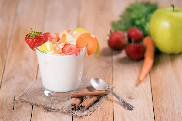 yogurt with strawberries apples and carrot in a glass on a wooden table