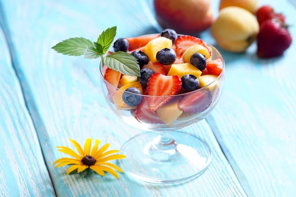 Slatky salade met een takje munt in de kom van glas. Blauwe achtergrond. — Stockfoto