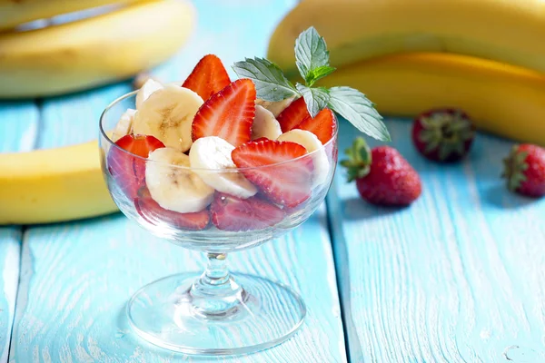 Salade met aardbeien en bananen met muntblaadjes. Blauwe achtergrond. — Stockfoto