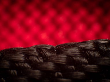 Yakın plan sentetik kumaş, siyah iplik. İplikler arasındaki küçük boşluklar, düzgün dokuma, büyük parlak lifler, yüksek büyütme, süper makro. Kırmızı ipliğin bulanık arkaplanı