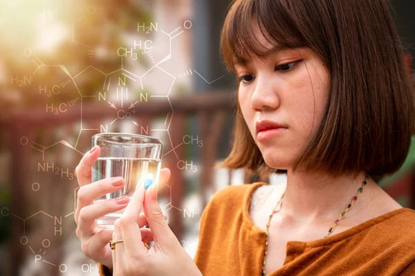 The woman who is sick with fever is sick, holding a glass of water in the right hand. Left hand holding a pill The background has a chemical bond.