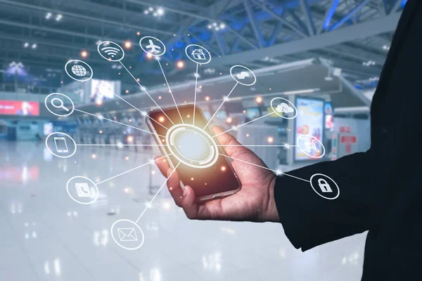 Takım elbiseli adam cep telefonunu sağ eliyle turuncu ışıkta tutuyor ve çevrimiçi uygulamalar, yer ayırtma, rezervasyon uçuşları, bilgisayar alışverişi için sembol taşıyor. Terminal bulanık